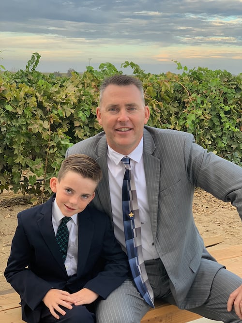 Matt Stoll and his son wearing suits with farmland behind them