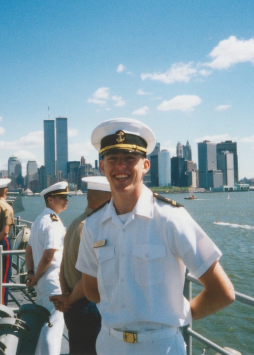 Matt Stoll posing on a boat in his dress uniform with new york city skyline behind him