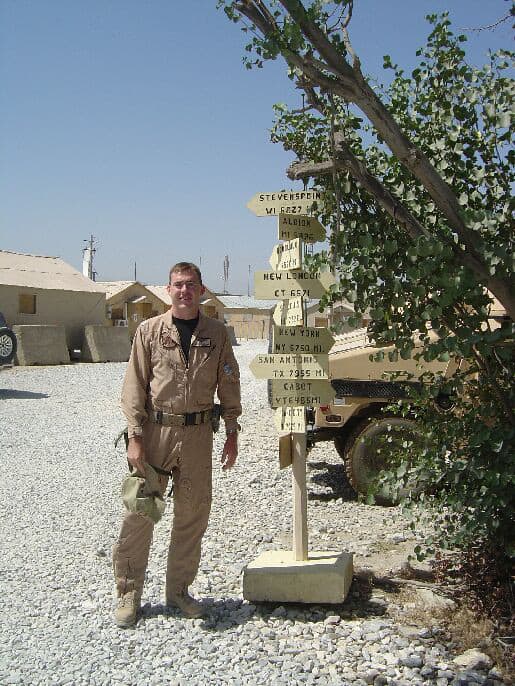 Matt Stoll in uniform standing next to a sign on a base in Afghanistan