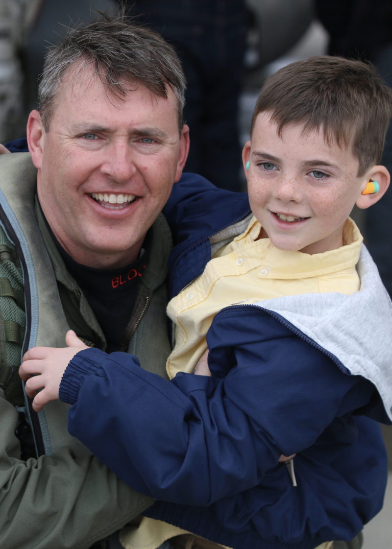 Matt Stoll in his flight suit smiling with his young son
